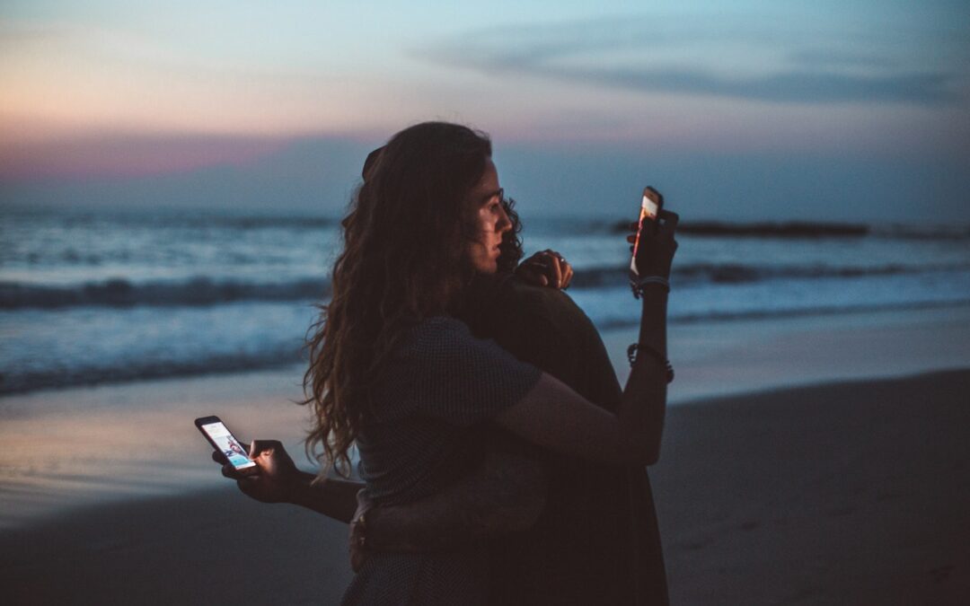 A couple hugging each other while looking at their smartphones