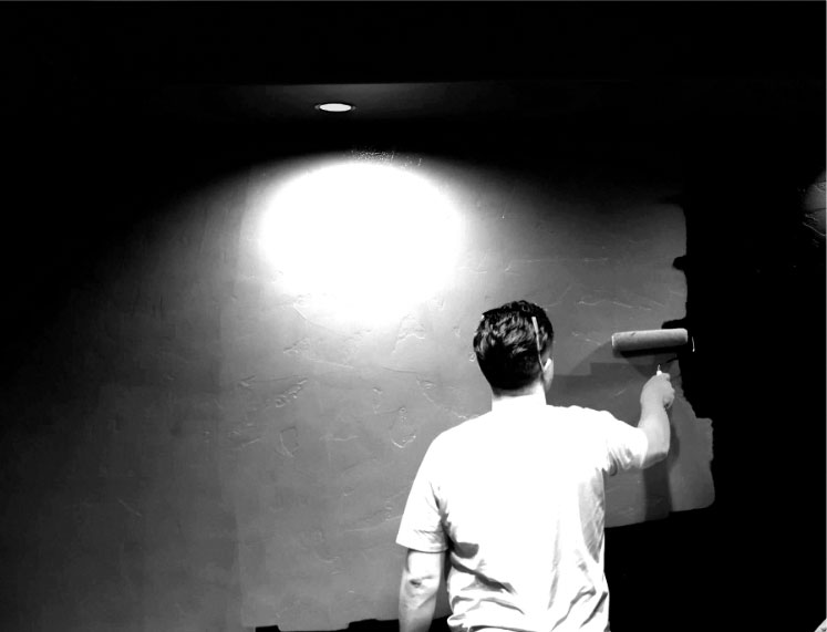 Black and White photo of man using a roller to paint with spotlight